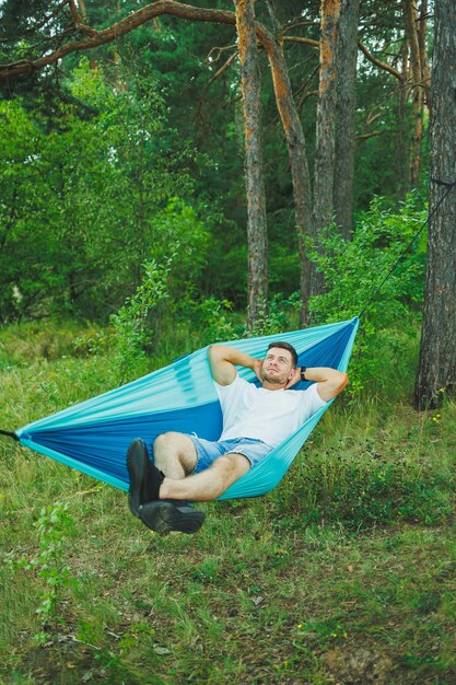 Un giovane uomo riposa nella natura seduto su un'amaca turistica Amaca per attività ricreative all'aperto Riposo del fine settimana di un uomo solitario in una foresta deserta