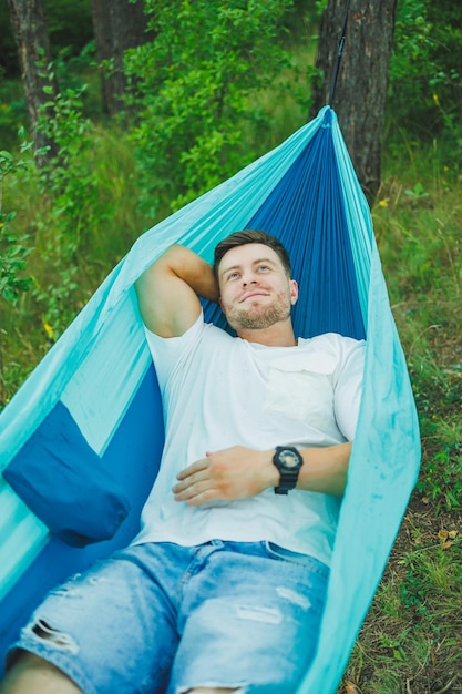 Un giovane uomo riposa nella natura seduto su un'amaca turistica Amaca per attività ricreative all'aperto Riposo del fine settimana di un uomo solitario in una foresta deserta