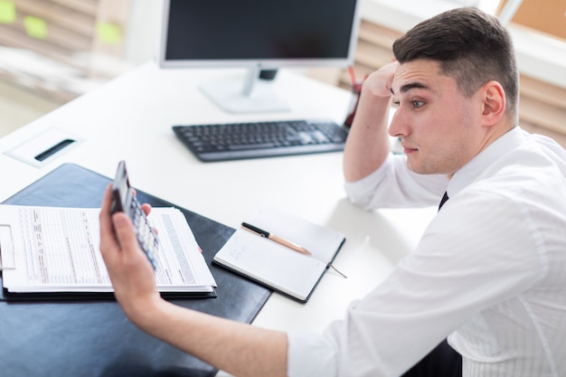 Un giovane uomo seduto a una scrivania del computer in ufficio e guardando la calcolatrice.