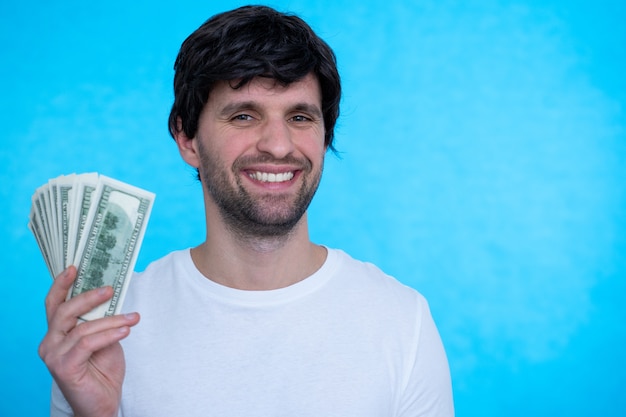 Un giovane uomo sicuro bello sta tenendo i dollari nelle sue mani felicemente