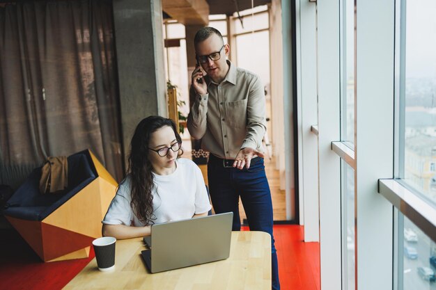 Un giovane uomo soddisfatto parla con una collega e si rallegra del lavoro svolto I colleghi lavorano al computer portatile in ufficio Lavorano in un ufficio moderno