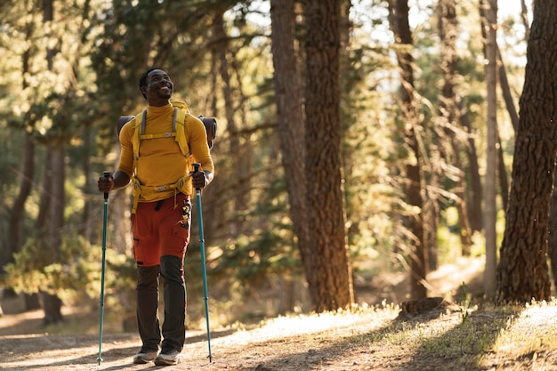 Un giovane viaggiatore afroamericano con uno zaino che cammina nella foresta è tra gli alberi un uomo con un grande zaino turistico che viaggia attraverso il concetto di ecoturismo della foresta