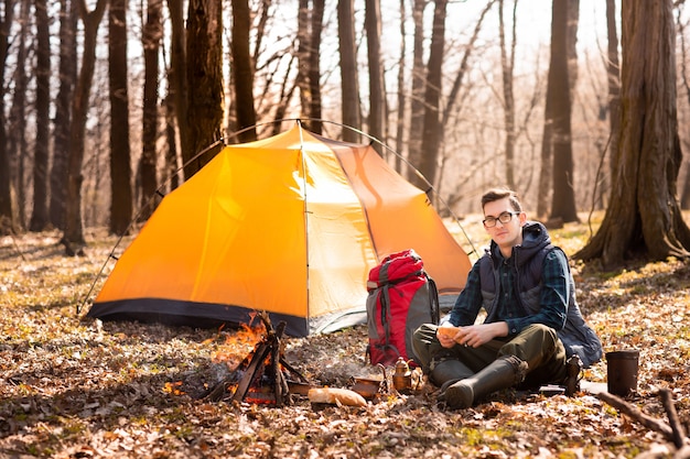 Un giovane viaggiatore nella foresta sta riposando vicino alla tenda e ha cucinato la colazione nella natura