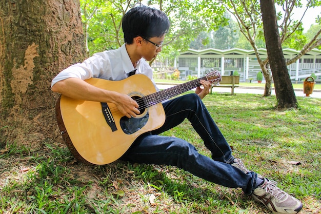 Un giovane vietnamita che suona la chitarra vicino a un grande albero nel giardino