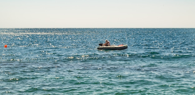 Un gommone guasto con un motore, un uomo accende il motore, un giorno d'estate in un mare calmo.