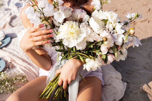 Un grande bouquet di peonie e campanelle bianche nelle mani di una ragazza in abito leggero