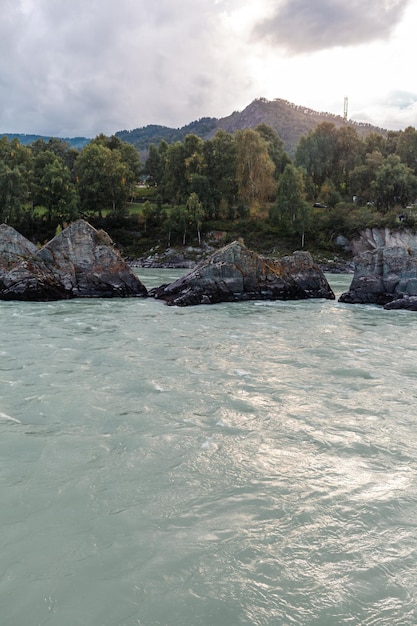 Un grande fiume di montagna che scorre veloce, ampio e pieno. Grandi rocce sporgono dall'acqua.