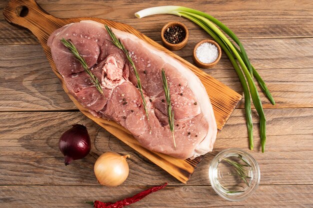 Un grande pezzo crudo di carne di maiale al vapore su un tagliere e un tavolo di legno con spezie vista dall'alto in stile rustico