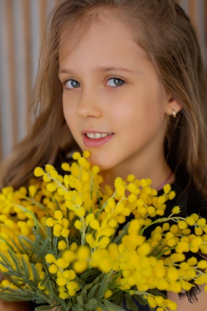 un grande ritratto di una ragazza dai capelli castani con un bouquet di mimosa tra le mani