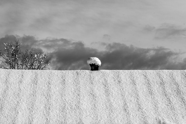 Un grande tetto di una casa con un piccolo camino coperto di neve contro un cielo nuvoloso nuvoloso scuro, foto in bianco e nero