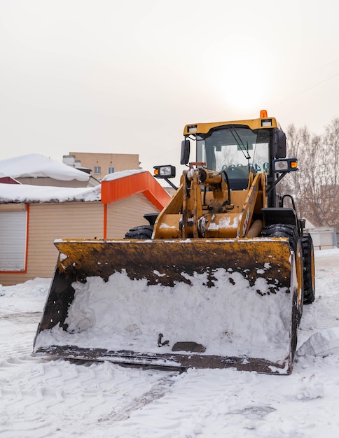 Un grande trattore giallo rimuove la neve dalla stradaPulizia delle strade della città dalla neve in inverno