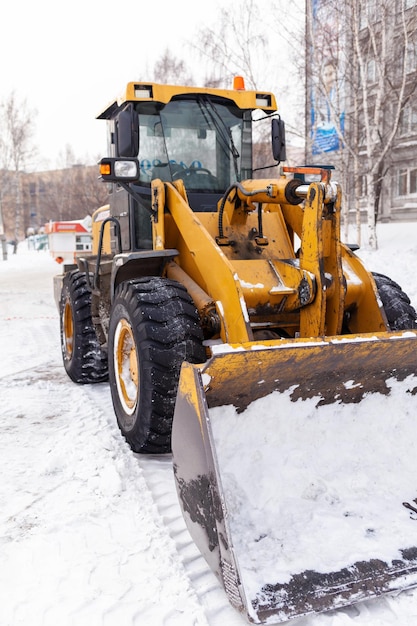 Un grande trattore giallo rimuove la neve dalla stradaPulizia delle strade della città dalla neve in inverno