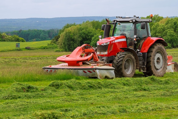 Un grande trattore rosso con due falciatrici falcia l'erba verde su un silo.