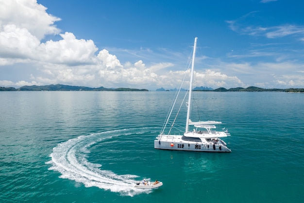 Un grande yacht a vela bianco e una barca a motore con persone.