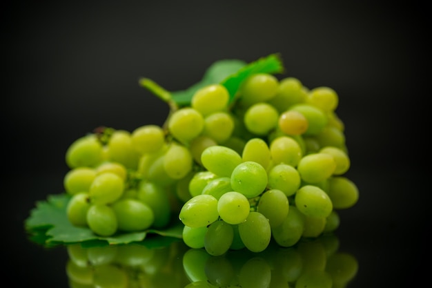 Un grappolo d'uva verde matura con foglie isolate su sfondo nero