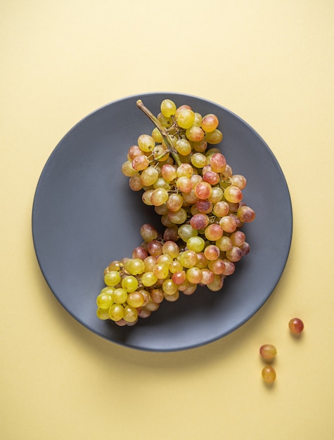 Un grappolo di succosa uva rosa verde in un piatto grigio