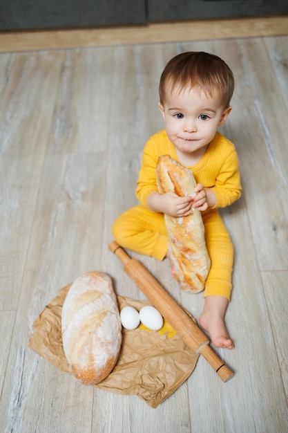 Un grazioso bambino di 1 anno è seduto in cucina e mangia pane fresco Bambino con il pane sul pavimento