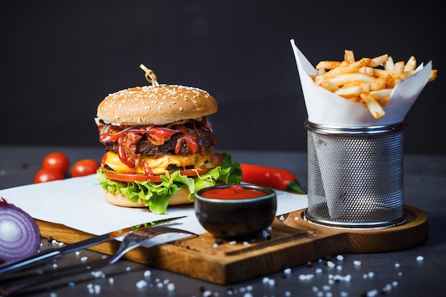 un grosso hamburger con patatine fritte sul tavolo scuro