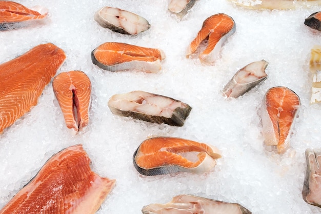 Un grosso pezzo di bistecca di salmone atlantico crudo e un altro pesce su un pezzo di ghiaccio bianco sgualcito