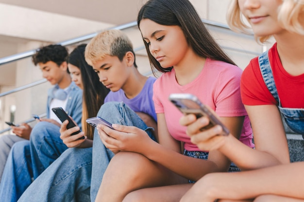 Un gruppo di adolescenti con telefoni cellulari che guardano la comunicazione video online seduti per strada