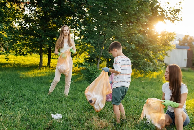 Un gruppo di adulti e bambini insieme al tramonto è impegnato nella raccolta dei rifiuti nel parco Riciclaggio dei rifiuti di tutela ambientale Smistamento dei rifiuti