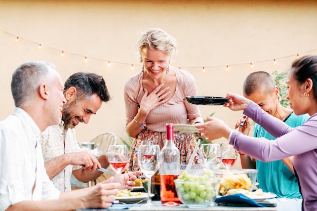 Un gruppo di amici adulti che condividono il cibo in una festa barbecue che si incontra con cibo e bevande a tavola