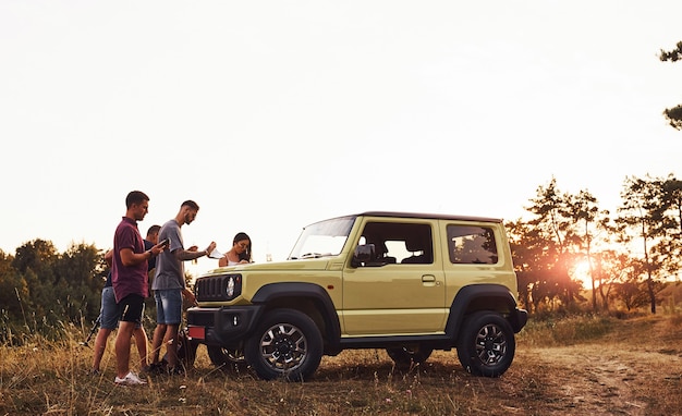 Un gruppo di amici allegri ha un bel fine settimana in una giornata di sole vicino alla loro macchina verde all'aperto