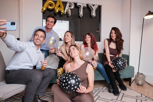 Un gruppo di amici che fanno un selfie sul divano a casa festeggiando insieme.
