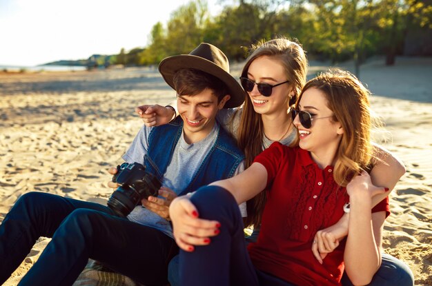 Un gruppo di amici che si godono il tempo sulla spiaggia. Ridono e sorridono. Atmosfera amichevole. I ragazzi amano le foto. Bene passare l'estate. Il sole al tramonto