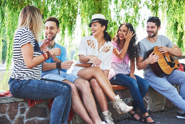 Un gruppo di amici felici con la chitarra mentre uno di loro suona la chitarра e gli altri lo applaudono