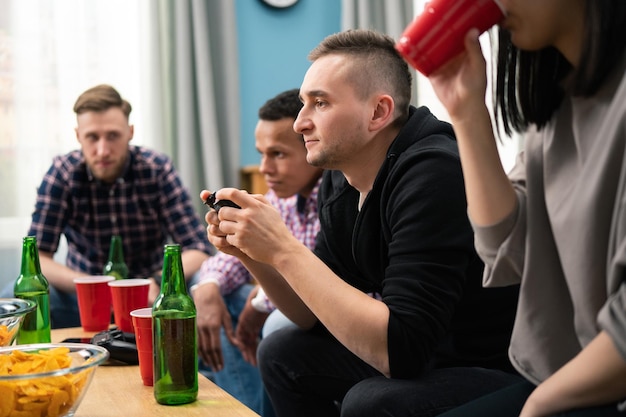 Un gruppo di amici gioca insieme ai videogiochi a casa divertendosi un uomo concentrato compete con un amico