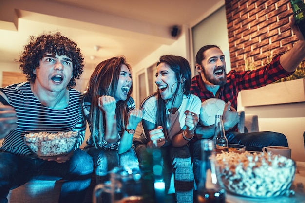 Un gruppo di amici guarda la trasmissione di un evento sportivo. Si siedono davanti alla TV in soggiorno, mangiano snack, bevono birra e fanno il tifo per la squadra del cuore.