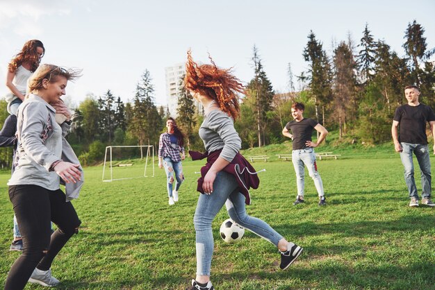 Un gruppo di amici in abito casual gioca a calcio all'aria aperta. Le persone si divertono e si divertono. Riposo attivo e tramonto scenico