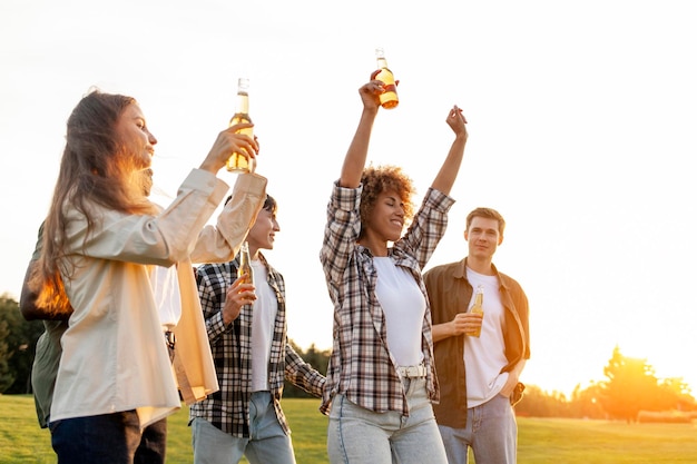 un gruppo di amici multirazziali a una festa con bottiglie di birra che ballano e si divertono all'aperto