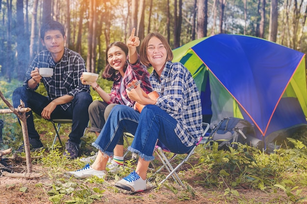 Un gruppo di amici si diverte con una bevanda calda e suona l&#39;ukulele accanto alla tenda.