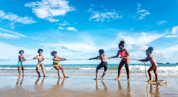 Un gruppo di bambini che tirano la corda e che fanno concorrenza sulla spiaggia contro il cielo blu.