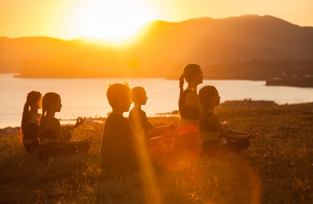 Un gruppo di bambini è impegnato nello yoga con un istruttore sull'oceano.