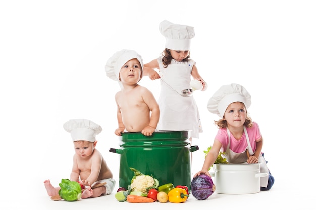 Un gruppo di bambini gioca e cucina con le verdure. Piccoli chef isolati su bianco, concetto di alimentazione sana