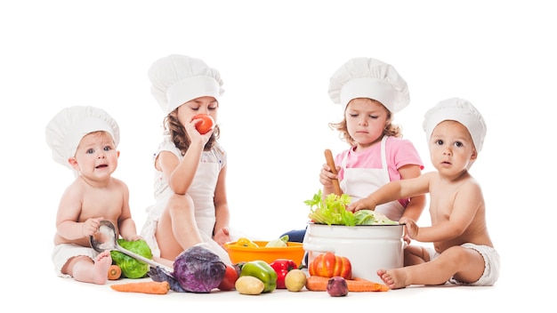 Un gruppo di bambini gioca e cucina con le verdure. Piccoli chef isolati su bianco, concetto di alimentazione sana