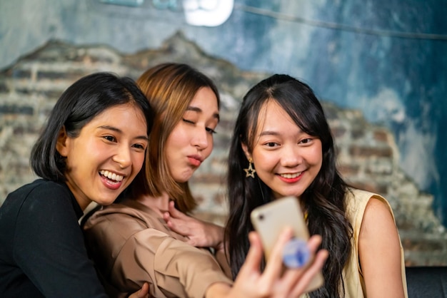 Un gruppo di belle amiche asiatiche che si incontrano e usano lo smartphone per fare un selfie insieme in un caffè amiche sorridenti che si godono lo stile di vita delle attività del fine settimana al caffè insieme con la felicità