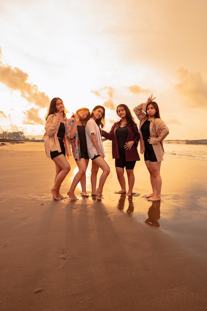 Un gruppo di donne asiatiche in camicie che posano felicemente mentre visitano una bellissima spiaggia