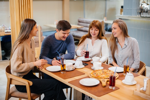 Un gruppo di giovani amici allegri è seduto in un bar a parlare e mangiare pizza. Pranzo in pizzeria.