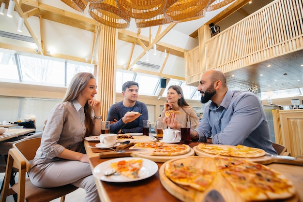 Un gruppo di giovani amici allegri è seduto in un bar a parlare e mangiare pizza. Pranzo in pizzeria.