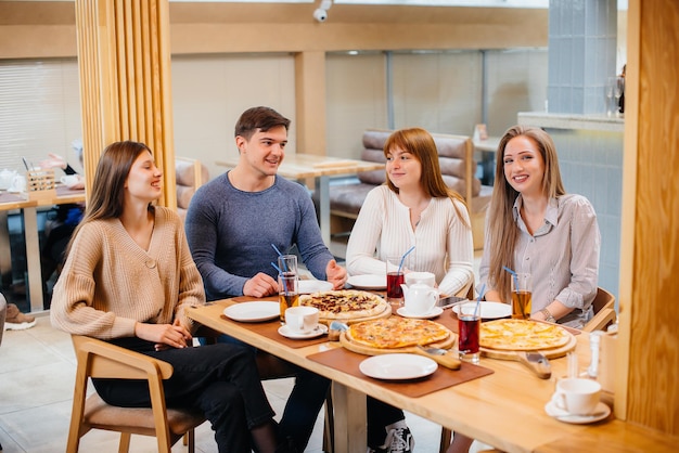 Un gruppo di giovani amici allegri è seduto in un bar a parlare e mangiare pizza. Pranzo in pizzeria.