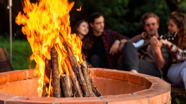 Un gruppo di giovani amici felici vicino a un falò al glamping. Due uomini e donne. Suonare la chitarra