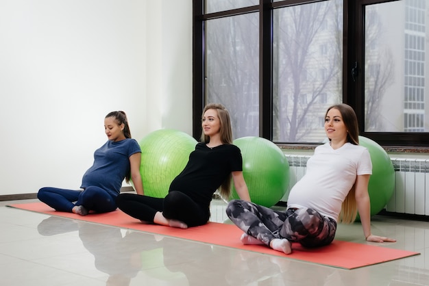 Un gruppo di giovani donne incinte fa yoga e sport su stuoie al coperto. Uno stile di vita sano