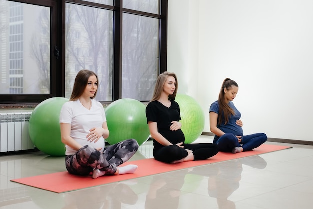 Un gruppo di giovani ragazze incinte fa yoga e sport su stuoie al coperto. Uno stile di vita sano.