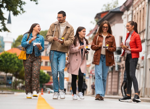 Un gruppo di giovani vestiti con abiti moderni parla mentre cammina per la città e mangia dolci Messa a fuoco selettiva Foto di alta qualità