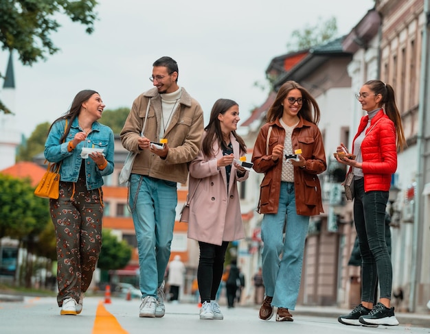 Un gruppo di giovani vestiti con abiti moderni parla passeggiando per la città e mangiando dolci. Messa a fuoco selettiva. Foto di alta qualità. Foto di alta qualità