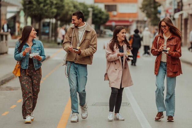 Un gruppo di giovani vestiti con abiti moderni parla passeggiando per la città e mangiando dolci. Messa a fuoco selettiva. Foto di alta qualità